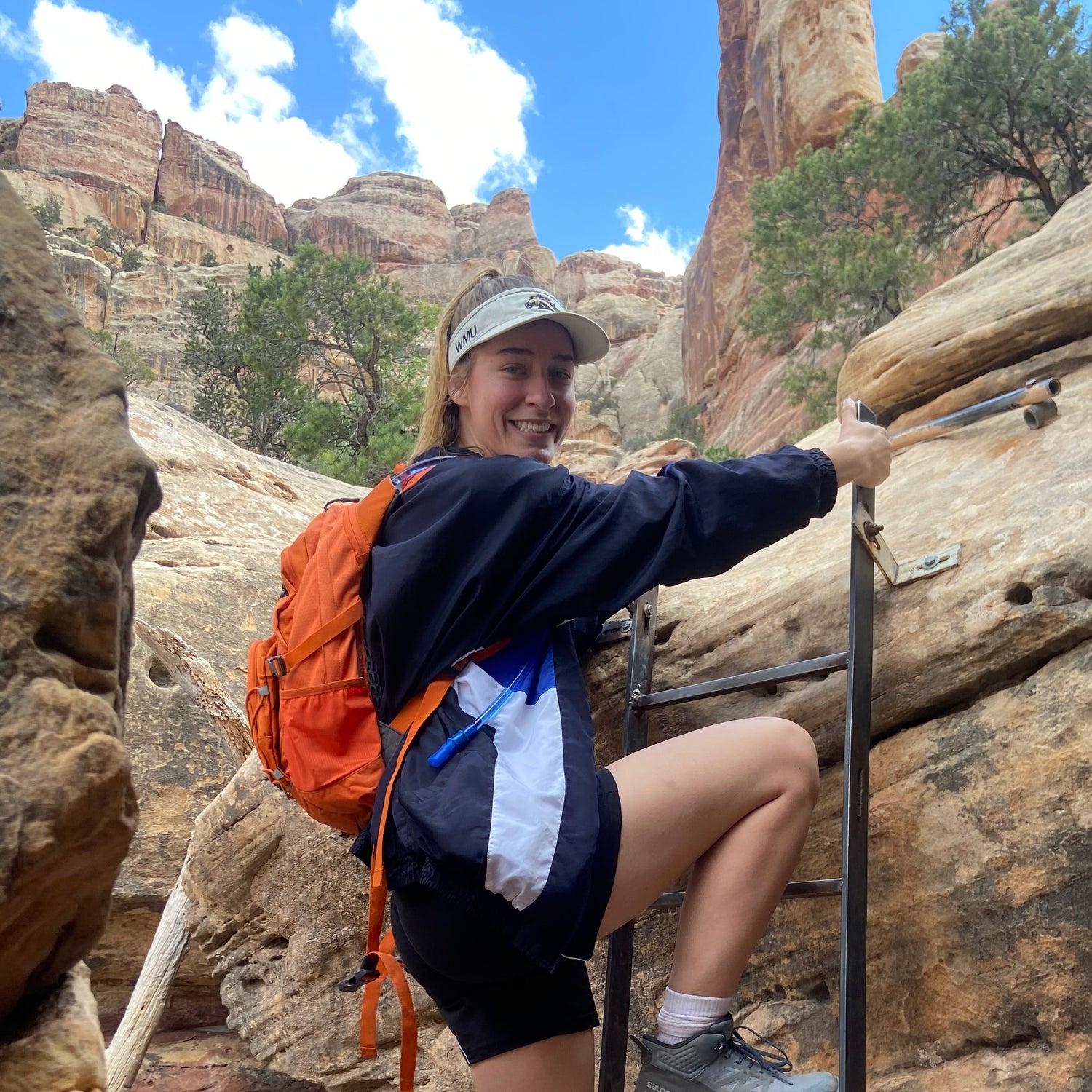Person climbing a rock face with a backpack and helmet on a sunny day.