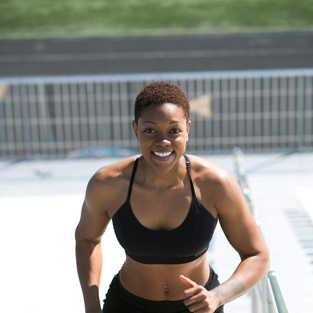Athlete in black sports bra and shorts standing on a track, giving a thumbs-up.