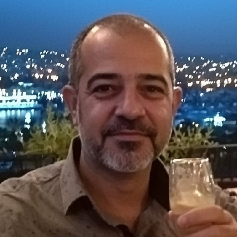 Man with a beard holding a glass against a cityscape at night